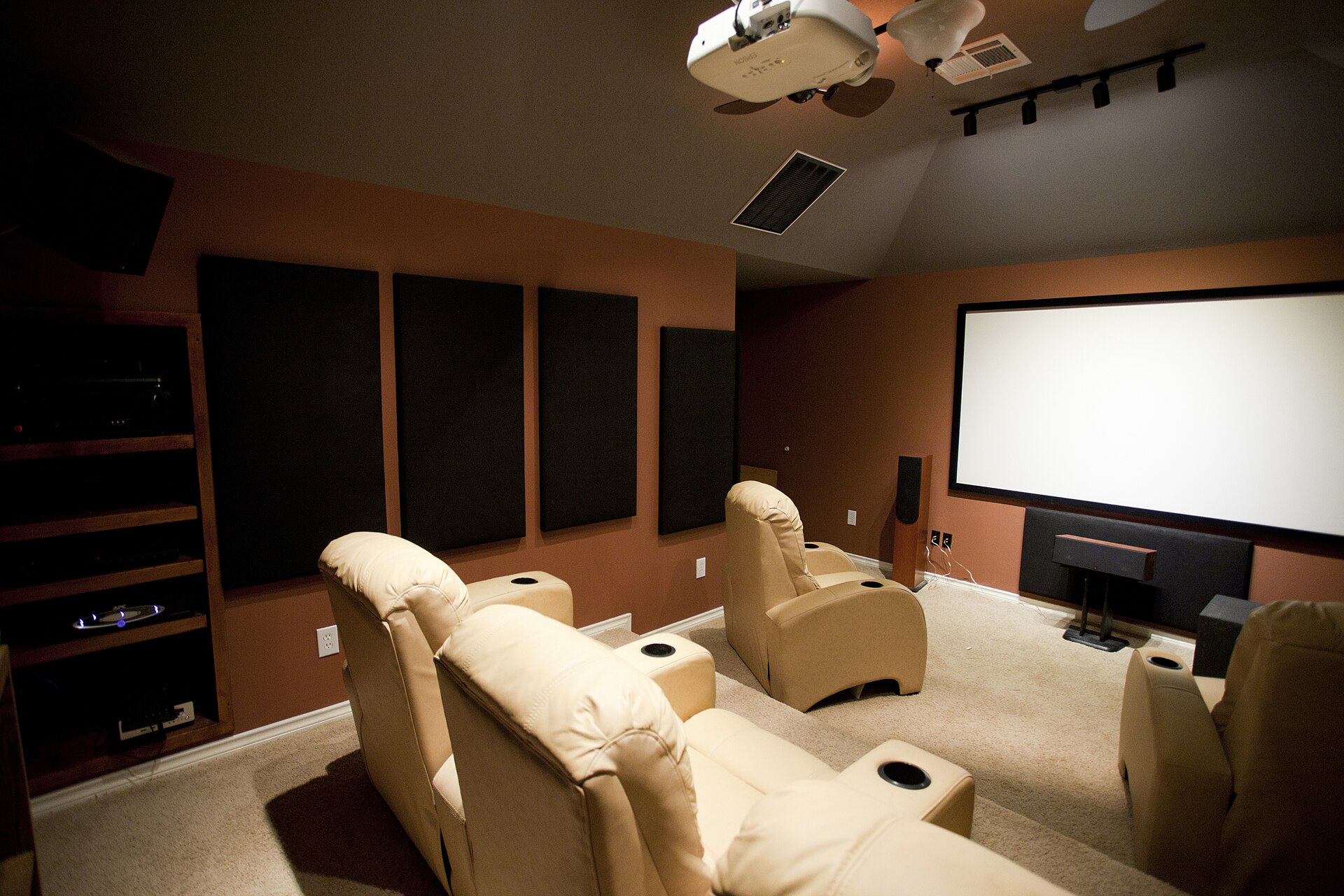 A dedicated cinema room with acoustic absorption panels on the side walls, a ceiling-mounted projector, a fixed-frame screen and two rows of tiered recliners